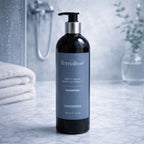 Remalisse Deep Cleanse Purify & Hydrate Shampoo in a black pump bottle with blue-grey label, standing on a cool-toned marble bathroom surface with soft, blurred background.