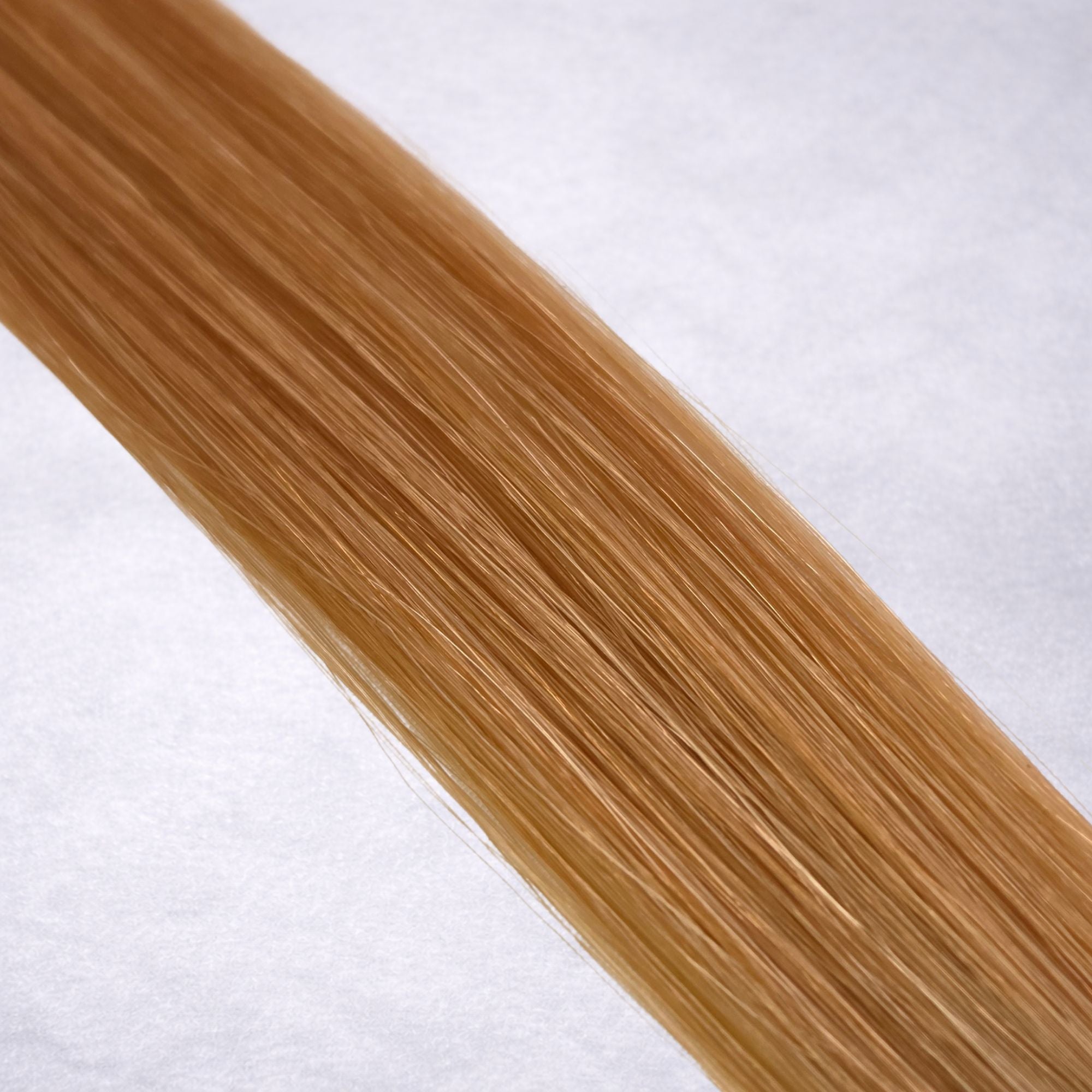 Luxury Remy human hair extension shade swatch in Strawberry Blonde #27 from the Remalisse Studio Collection, featuring a warm copper blonde tone with soft rosy-golden undertones, natural dimension, a silky finish, and natural shine.