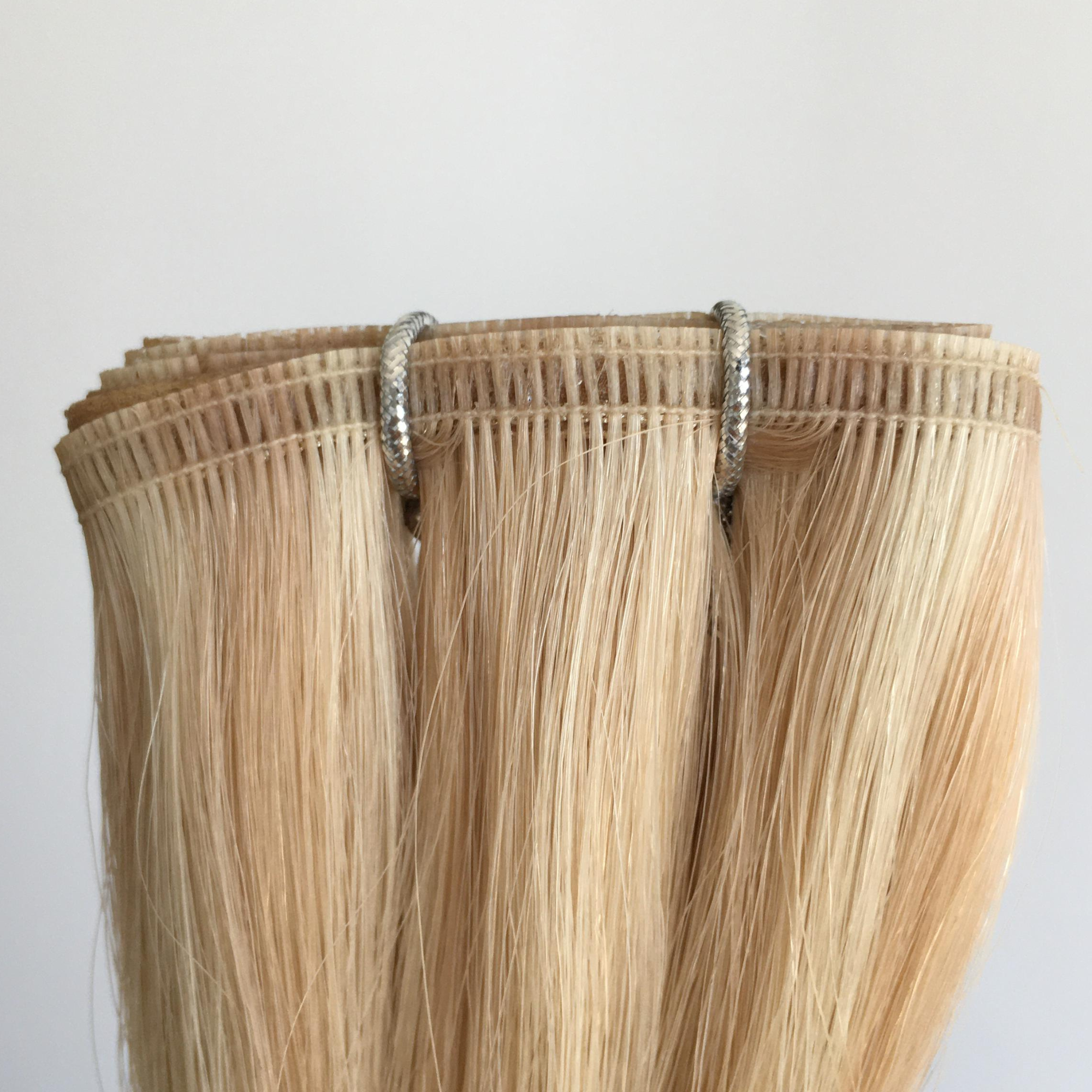 Close -up of Remalisse Studio Flat Weft hair extensions in a light blonde shade, showing the seamless flat weft edge and stitching detail on a white background. 