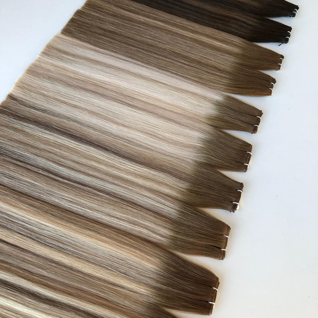 Close up of Remalisse Studio Flat Weft hair extensions in multiple brunette and blonde shades displayed on a white background, showing the seamless flat weft edge and colour variation.