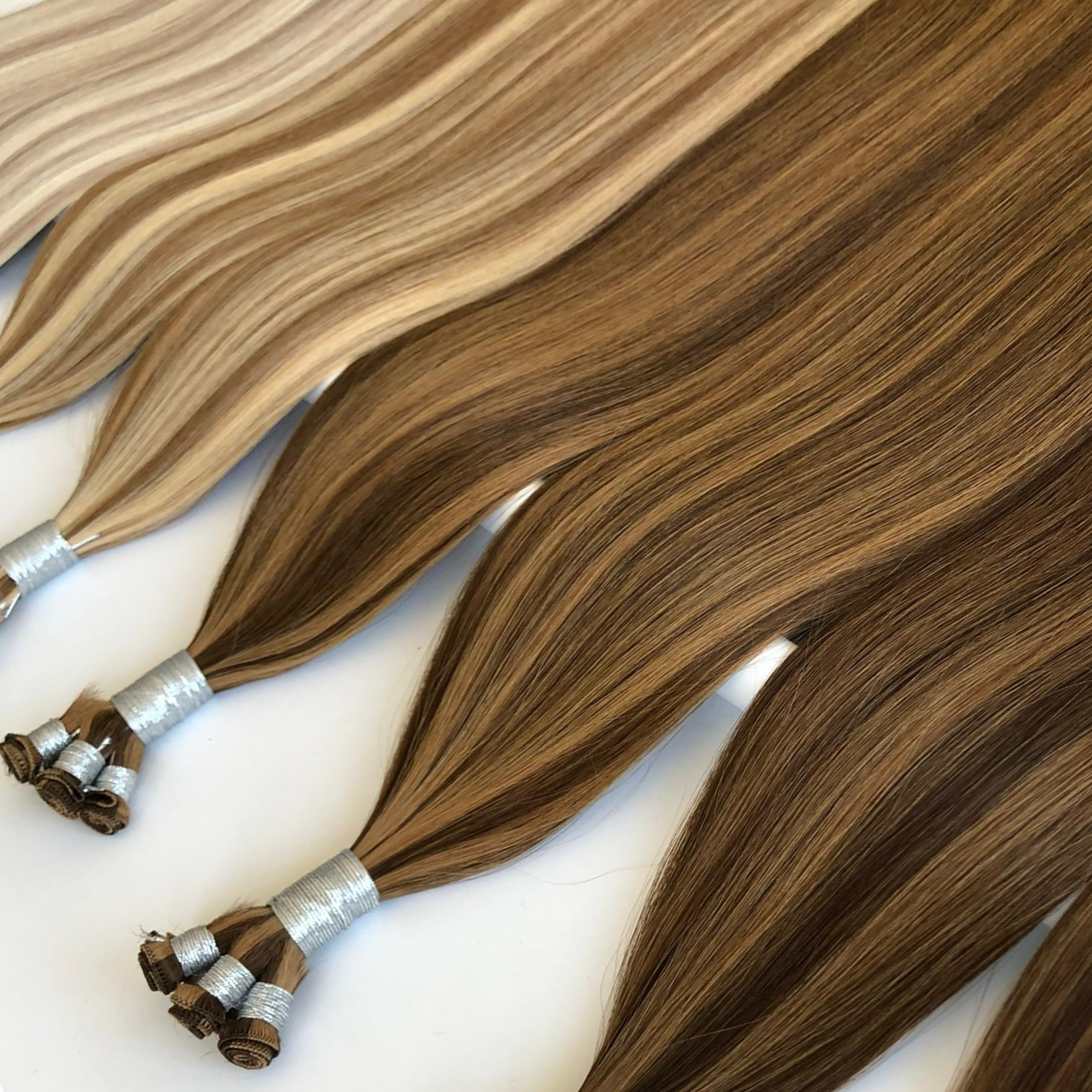 Studio hand tied weft hair extensions in blonde and brown balayage shades on white background