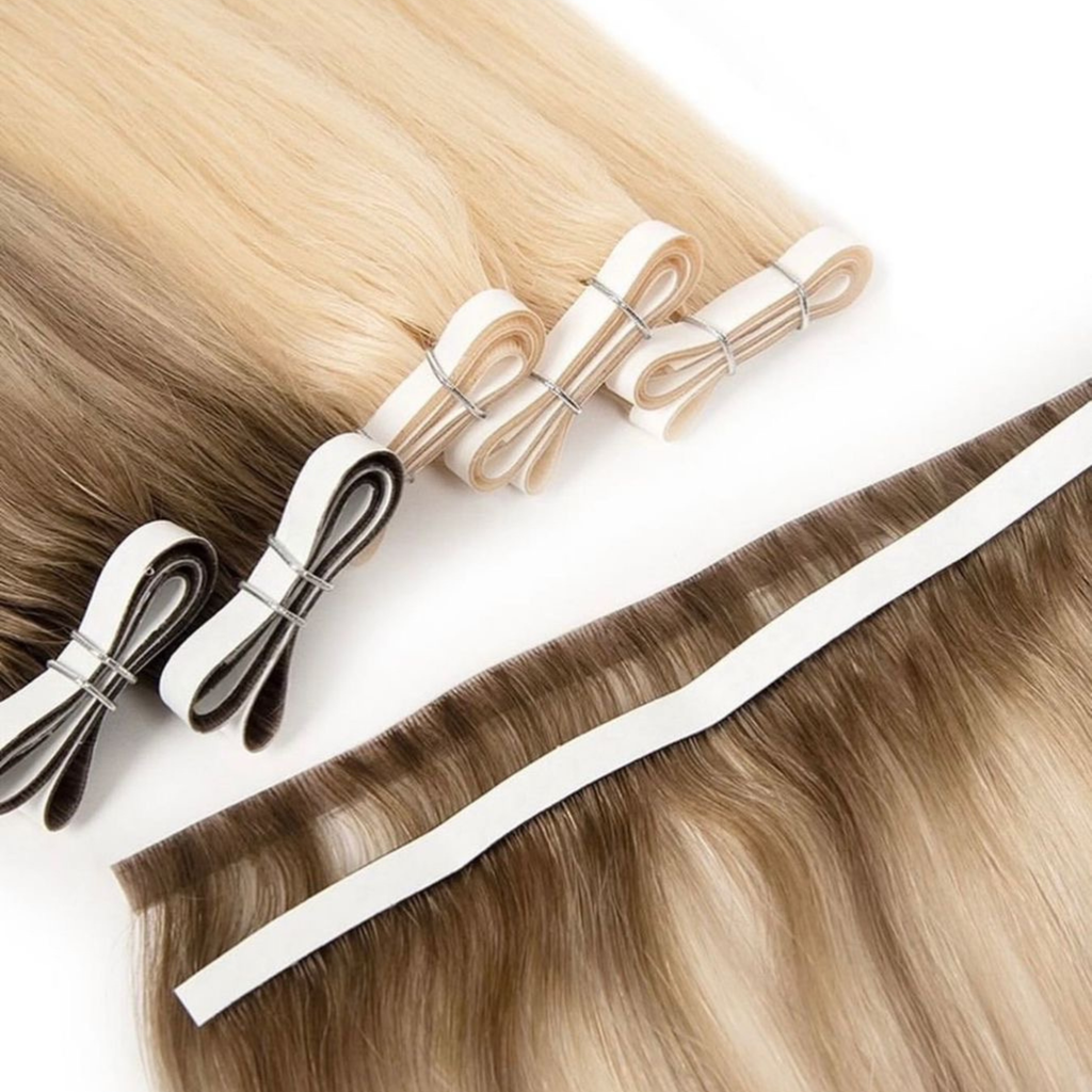 Close-up of blonde and brunette invisible tape weft hair extensions displayed alongside matching tape sections. The Remy human hair features soft blended tones with ultra-flat adhesive tape wefts designed for a seamless, scalp-like finish against a clean white background.