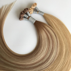 Close-up of blonde keratin bond hair extensions arranged in a curved layout, featuring silky Remy human hair and keratin fusion tips. The strand-by-strand extensions showcase smooth texture, glossy shine and seamless professional bond construction against a clean white background.