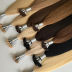 Close-up of keratin bond hair extensions displayed in multiple blonde, brunette and dark shades. The strand-by-strand Remy human hair extensions feature keratin fusion tips with a silky smooth texture and glossy finish arranged against a clean white background.