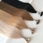 Close-up of Studio keratin bond hair extensions in multiple shades, featuring strand-by-strand Remy human hair with keratin fusion tips. The silky extensions display black, brunette, blonde and icy blonde tones with smooth texture and glossy finish against a clean light background.