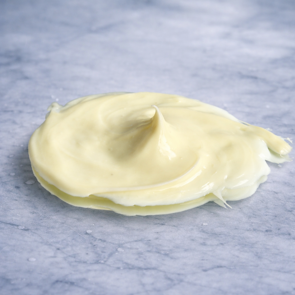 Close-up of a smooth, pale yellow cream dollop with a soft peak, placed on an icy blue marble surface with subtle veining and cool-toned lighting. 