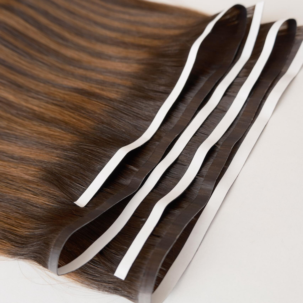 Close-up of dark brunette tape weft hair extensions with wide adhesive tape sections visible along the top. The Smooth Remy human hair has a sleek, glossy finish and  showcases the flat tape weft construction against a clean white background.