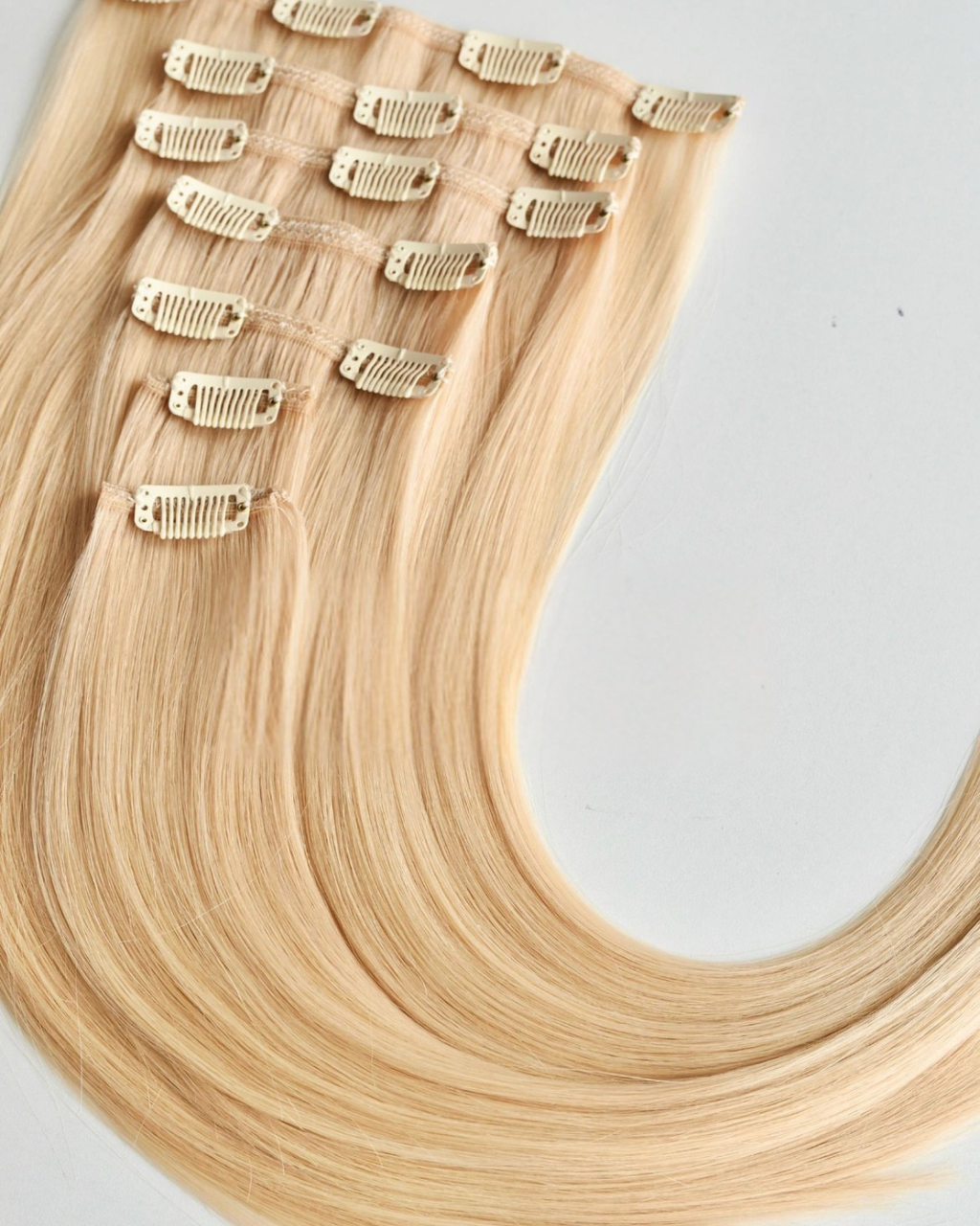 Studio Collection Remy human hair clip-in extensions in icy blonde shades, featuring seamless multi-piece clip wefts with lightweight discreet construction, silky smooth texture and natural salon-quality shine.