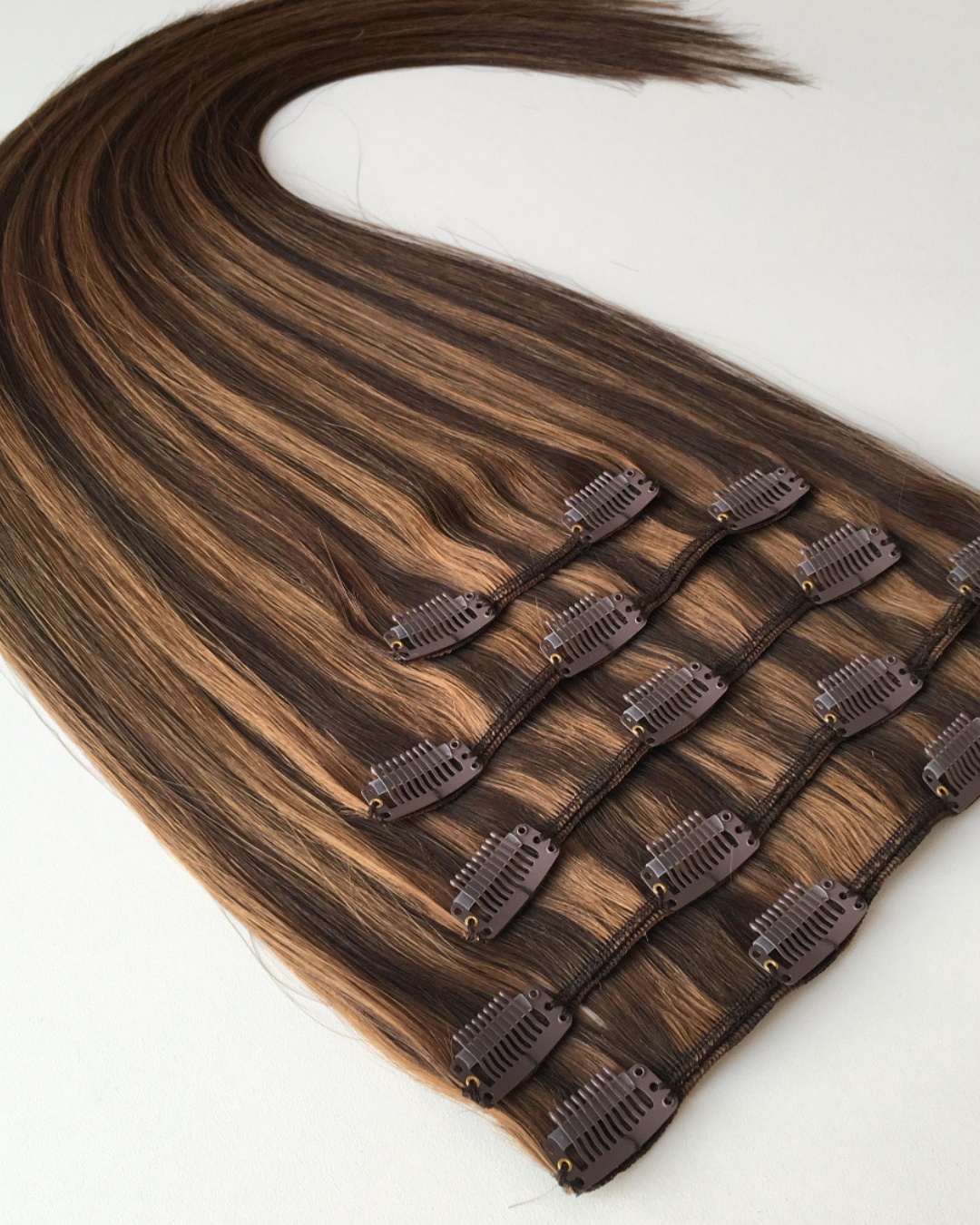 Studio Collection Remy human hair clip-in extensions in dimensional brunette balayage shades, featuring discreet multi-piece clip wefts with seamless lightweight construction, soft silky texture and natural shine.